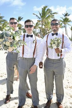 three men in suits and bow ties standing on the beach with palm trees behind them