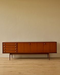 a wooden dresser sitting on top of a hard wood floor next to a white wall