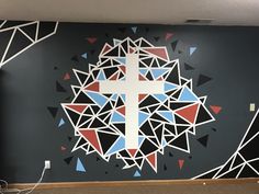 a cross painted on the side of a wall with geometric shapes and triangles around it