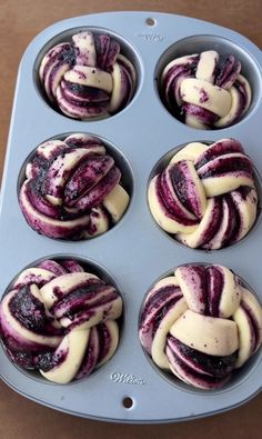 six cupcakes in a muffin tin with white frosting and purple swirl