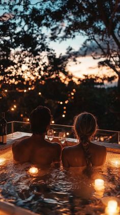 two people sitting in a hot tub with candles on the side and trees in the background