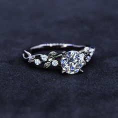 a diamond ring with leaves on it sitting on a black surface, in front of a dark background