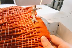 someone is using a sewing machine to sew on an orange fabric with white stitching