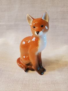 a small figurine of a little fox sitting on a white cloth covered surface