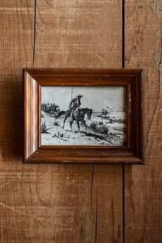 a framed drawing of a man on a horse riding through the desert in a wooden frame