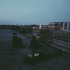 two people sitting on top of a roof next to each other in front of a cityscape