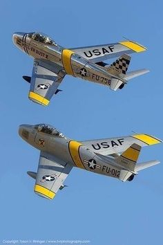 two fighter jets flying side by side in the blue sky with white and yellow markings