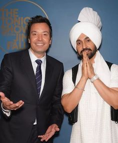 two men standing next to each other in front of a blue wall wearing turbans