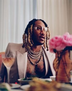 a man with dreadlocks sitting at a table in front of a pink flower