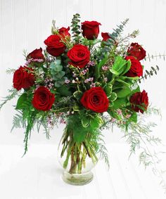 a vase filled with red roses and greenery