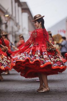 a woman in a red dress and hat is dancing with other people on the street