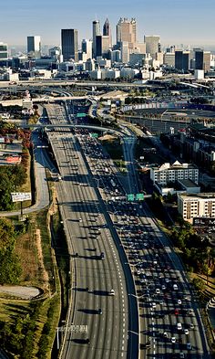 an aerial view of a highway with lots of traffic in the foreground and large cityscape in the background