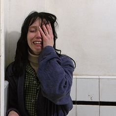 a woman holding her hand to her face while standing next to a white tiled wall