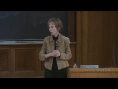 a woman standing in front of a blackboard giving a lecture at the college hall