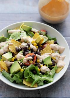 a salad with black beans, avocado, tomatoes and cheese on it in a white bowl