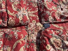 a red and gold floral comforter with blue tags on it