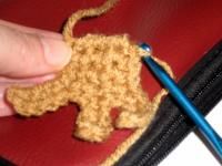 someone is crocheting an elephant on a red piece of cloth with a blue needle