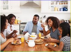 a group of people sitting around a wooden table eating food and drinking orange juices