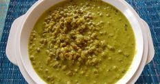 a white bowl filled with green soup on top of a blue mat