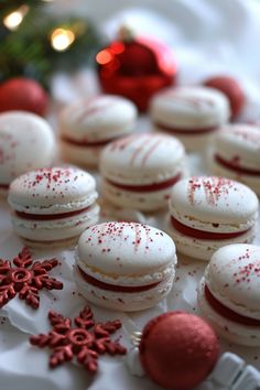 Festive white macarons with red filling, decorated with red sprinkles and surrounded by red ornaments and snowflakes. Christmas Confectionary Ideas, Fancy Christmas Baking, Macaroon Gift, Christmas Confections, Christmas Macarons Recipe, Macarons Christmas, Xmas Macarons