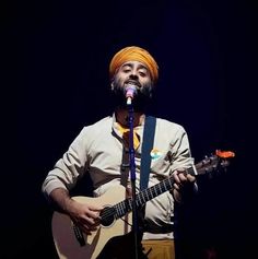 a man with an orange turban is playing guitar and singing into a microphone