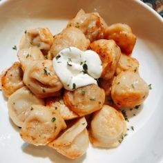 a white plate topped with dumplings covered in sour cream and garnished with parsley