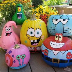 five painted pumpkins sitting on top of a wooden table next to flowers and plants