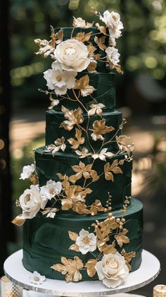 a green wedding cake with gold leaves and flowers on the top tier is decorated with white roses