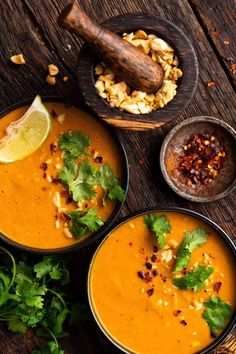 three bowls filled with soup and garnished with cilantro, pine nuts and lime