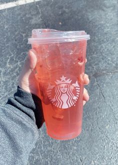 a person holding up a plastic cup with liquid in it's hand on the street