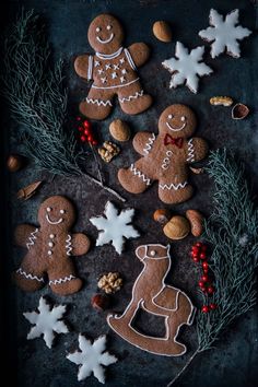 ginger cookies decorated with icing and christmas decorations on a slate board surrounded by fir branches