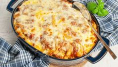 a casserole dish with meat and cheese in it on a blue cloth next to a spoon