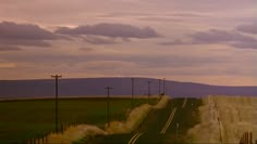 an empty road in the middle of a field with power lines and telephone poles on either side