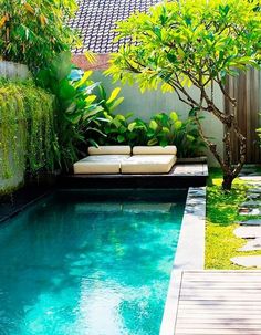 an outdoor swimming pool surrounded by greenery and wooden decking, with lounge chairs on the side