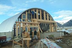 two men are standing in front of a building that is being built with wooden framing