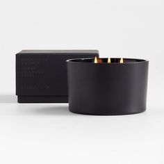 a black candle holder with three candles in it and a box behind it on a white surface