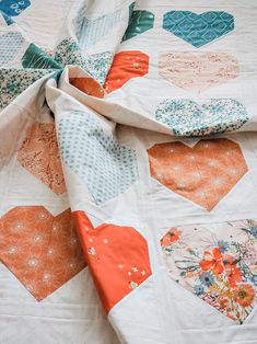 an orange and blue heart quilt on top of a white bed sheet with hearts printed on it