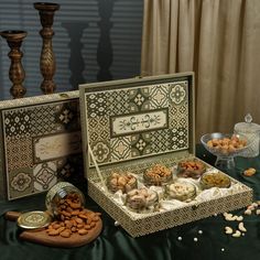 an assortment of nuts and crackers in a box on a green table cloth next to wooden candlesticks