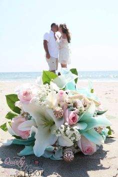 a bride and groom standing on the beach with their wedding bouquet in front of them