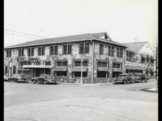 an old black and white photo of cars parked in front of a building with many windows