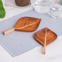 two wooden serving spoons on a placemat next to a glass of water and a plant