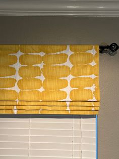 a yellow and white patterned roman blind hanging on the side of a window sill