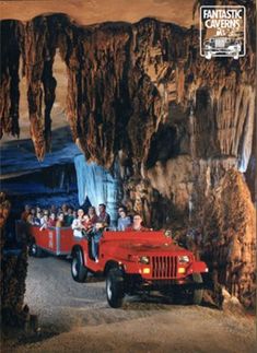 a red jeep driving through a cave filled with lots of people on top of it