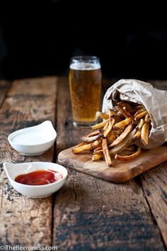 french fries and ketchup are sitting on a wooden table next to a glass of beer