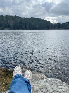 someone's feet resting on the edge of a rock near a body of water