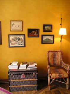 a living room with yellow walls and pictures on the wall next to a wicker chair