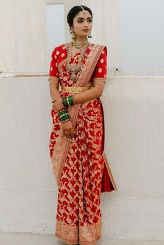 a woman in a red and gold sari standing next to a wall with her hands on her hips