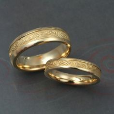 two yellow gold wedding rings with engraved designs on them, set against a gray background