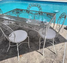 a glass table with four chairs next to a swimming pool