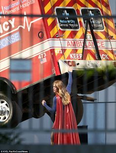 a woman in a red cape is standing next to a large truck that has the word emergency response painted on it